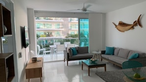 Un salon moderne avec un canapé, une table basse et un téléviseur. Il y a un balcon aménagé avec du mobilier d’extérieur.