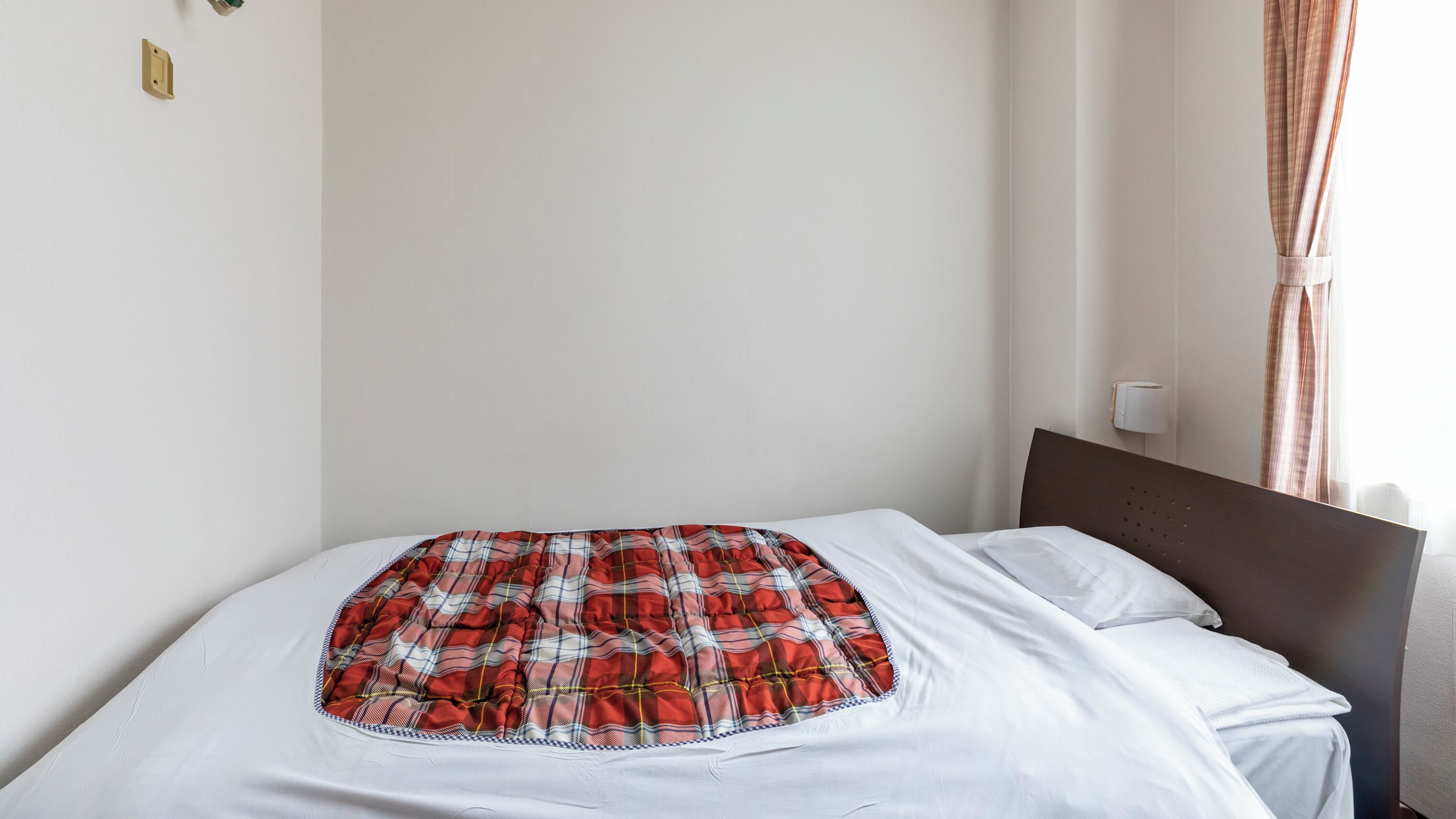 A bed with a plaid blanket, white sheets, and a headboard.