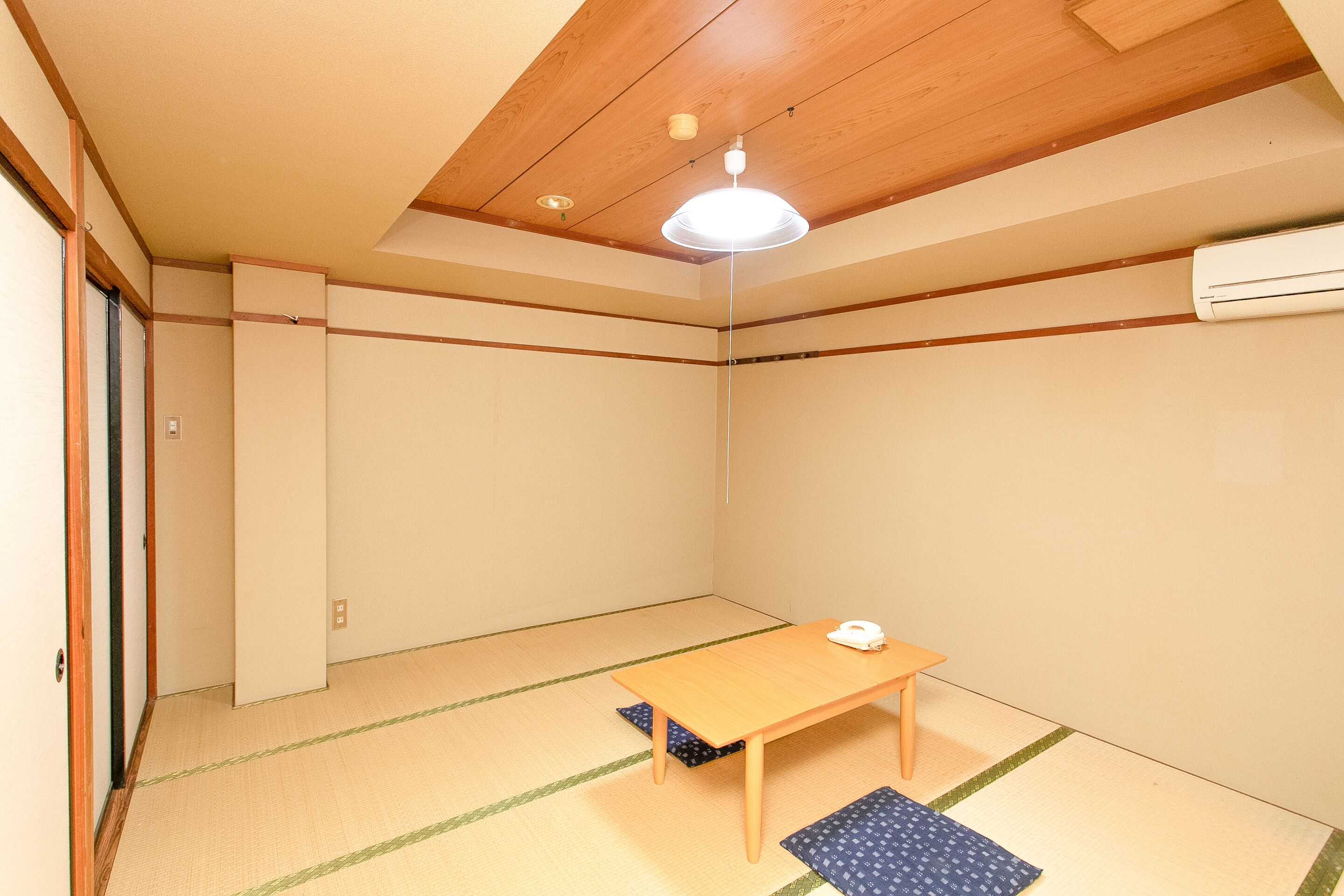 A room with tatami flooring, a wooden table, a ceiling light, and an air conditioning unit.