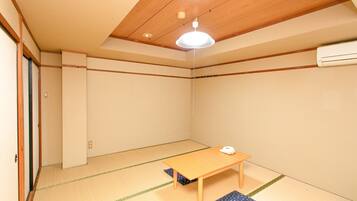 A room with tatami flooring, a wooden table, a ceiling light, and an air conditioning unit.