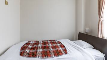 Una camera d'albergo con un letto, un condizionatore d'aria a parete, una parete spoglia e una finestra con tende.