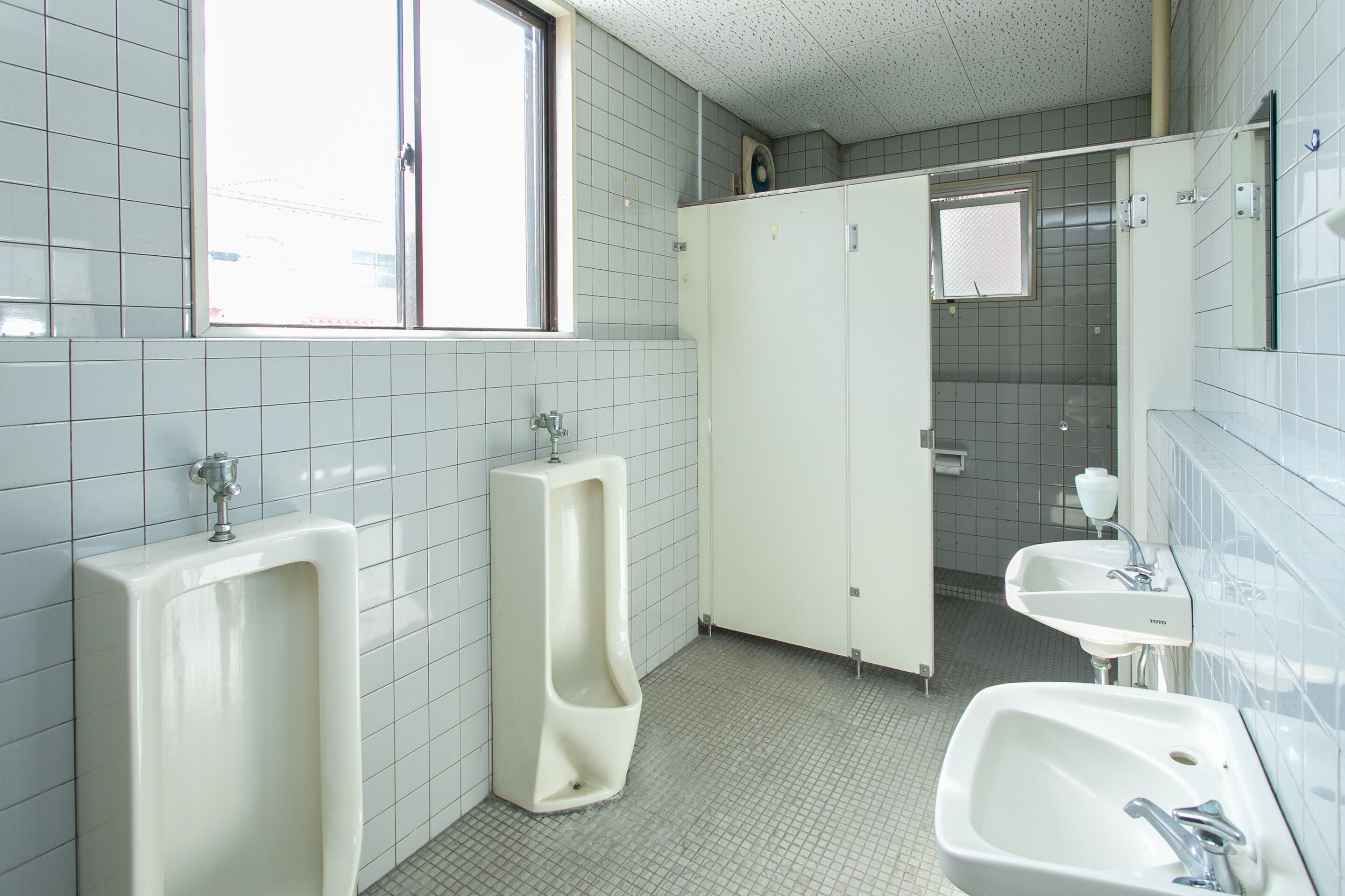 Een openbaar toilet met twee urinoen, een wastafel en een spiegel.