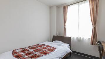 A single bed with a plaid blanket, a bedside table, a chair, and a window with curtains.