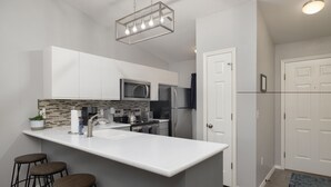 Une cuisine moderne avec un plan de travail blanc, des appareils en acier inoxydable et un luminaire suspendu.