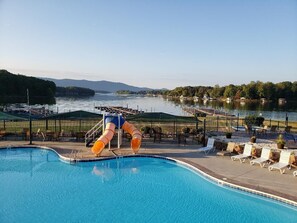Zwembad met glijbaan, ligbedden en uitzicht op een meer en bergen.