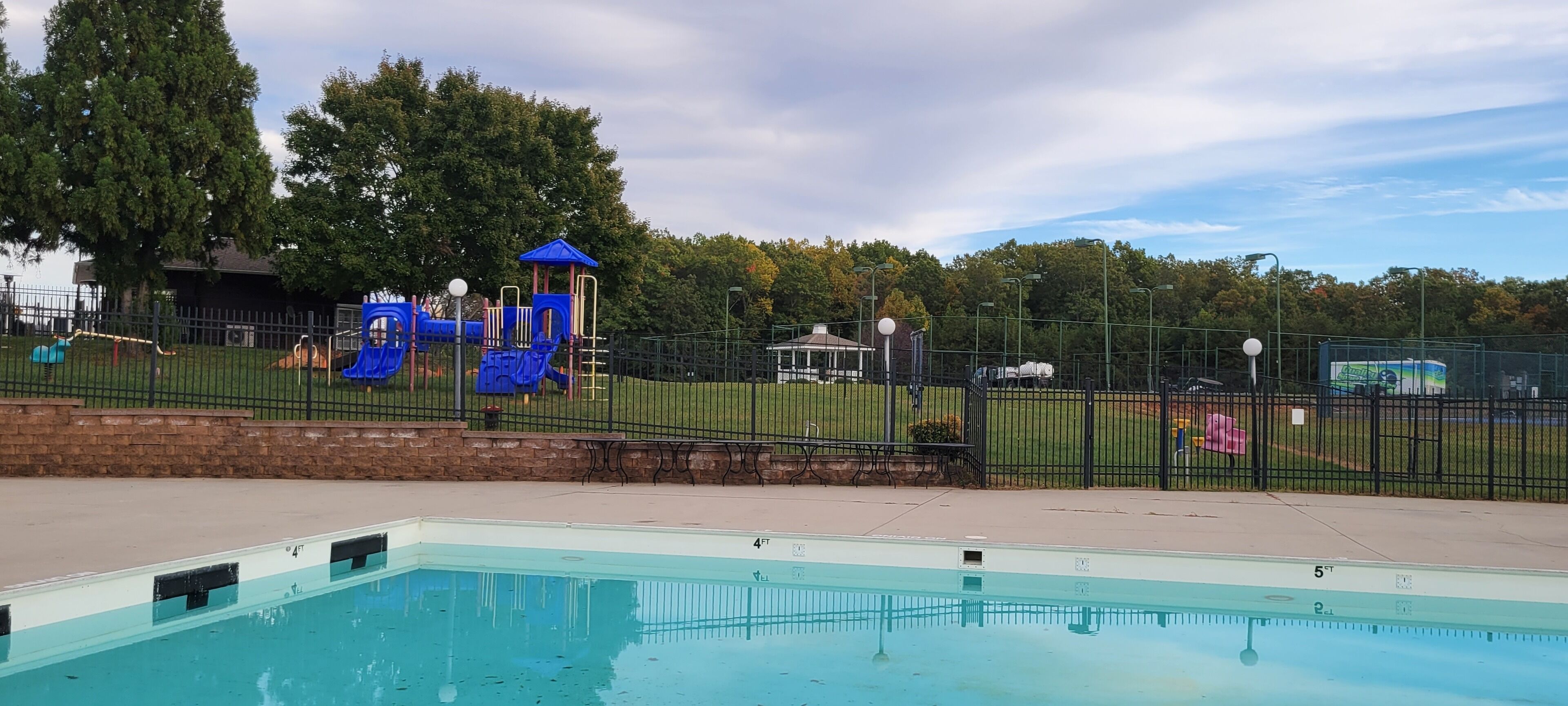 A swimming pool with a fenced playground area, a gazebo, and a picnic table.