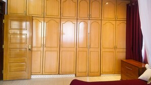 Une pièce comprenant une grande armoire en bois, un lit recouvert d’une courtepointe rouge et une petite table de chevet en bois.