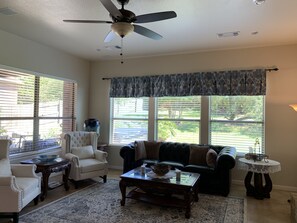 Una sala de estar con ventilador de techo, chimenea, sofá, mesa de centro y ventana con persianas.
