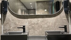 A modern bathroom with two sinks, a large mirror, and marble walls. - The Red Boat (Stockholm)