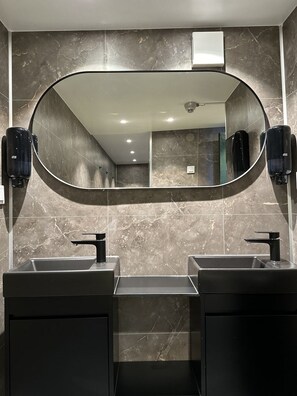 A modern bathroom with two sinks, a large mirror, and marble walls. - The Red Boat (Stockholm)