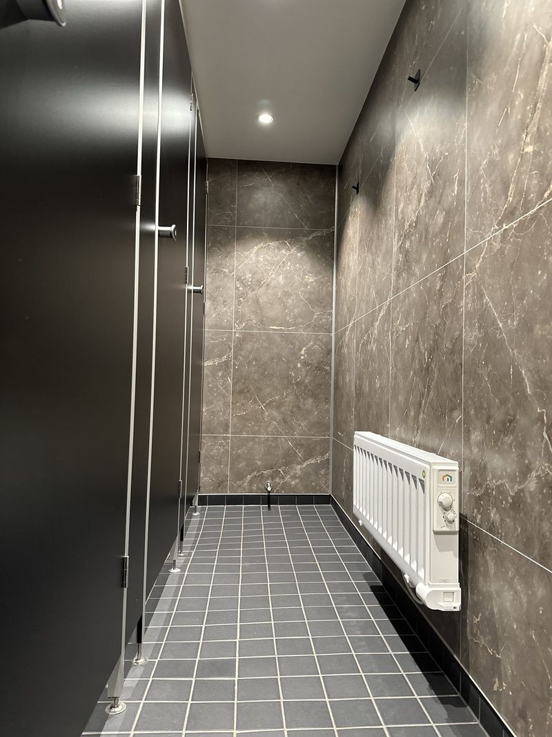 A modern bathroom with a shower, tiled floor, and a wall-mounted radiator.