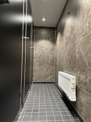 A modern bathroom with a shower, tiled floor, and a wall-mounted radiator. - The Red Boat (Stockholm)