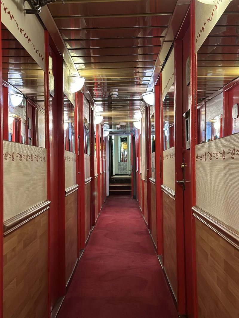 A corridor with red doors, a red carpet, and a ceiling with lights.