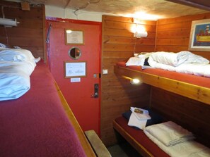 A cabin with bunk beds, a red door, and a small bench. - The Red Boat (Stockholm)