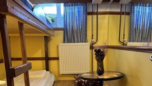 A bunk bed room with a round table and a radiator. - The Red Boat (Stockholm)