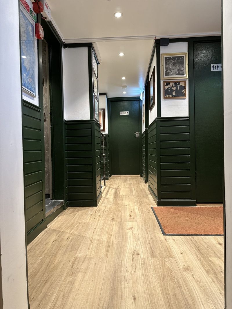 A hallway with wooden flooring, green walls, and a door at the end.
