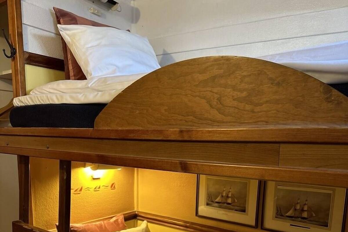A bunk bed with a wooden headboard, a small shelf, and a wall-mounted light.