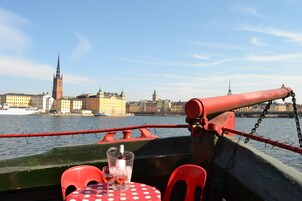 Una mesa con mantel de lunares y dos sillas rojas en un barco con vista a un paisaje urbano y un río.