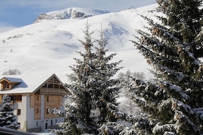 Un chalet de madera con balcón, rodeado de árboles cubiertos de nieve y una montaña al fondo.
