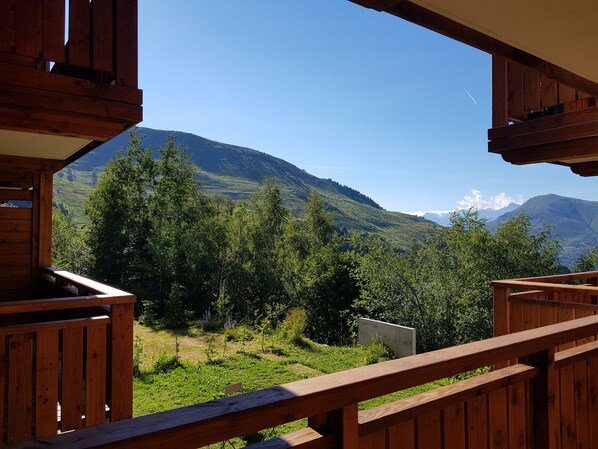 Un balcón de madera con vistas a un paisaje montañoso, con vegetación exuberante y cielo despejado.
