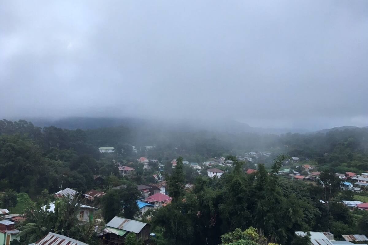 Uma aldeia com casas rodeada por uma floresta densa e montanhas ao fundo.