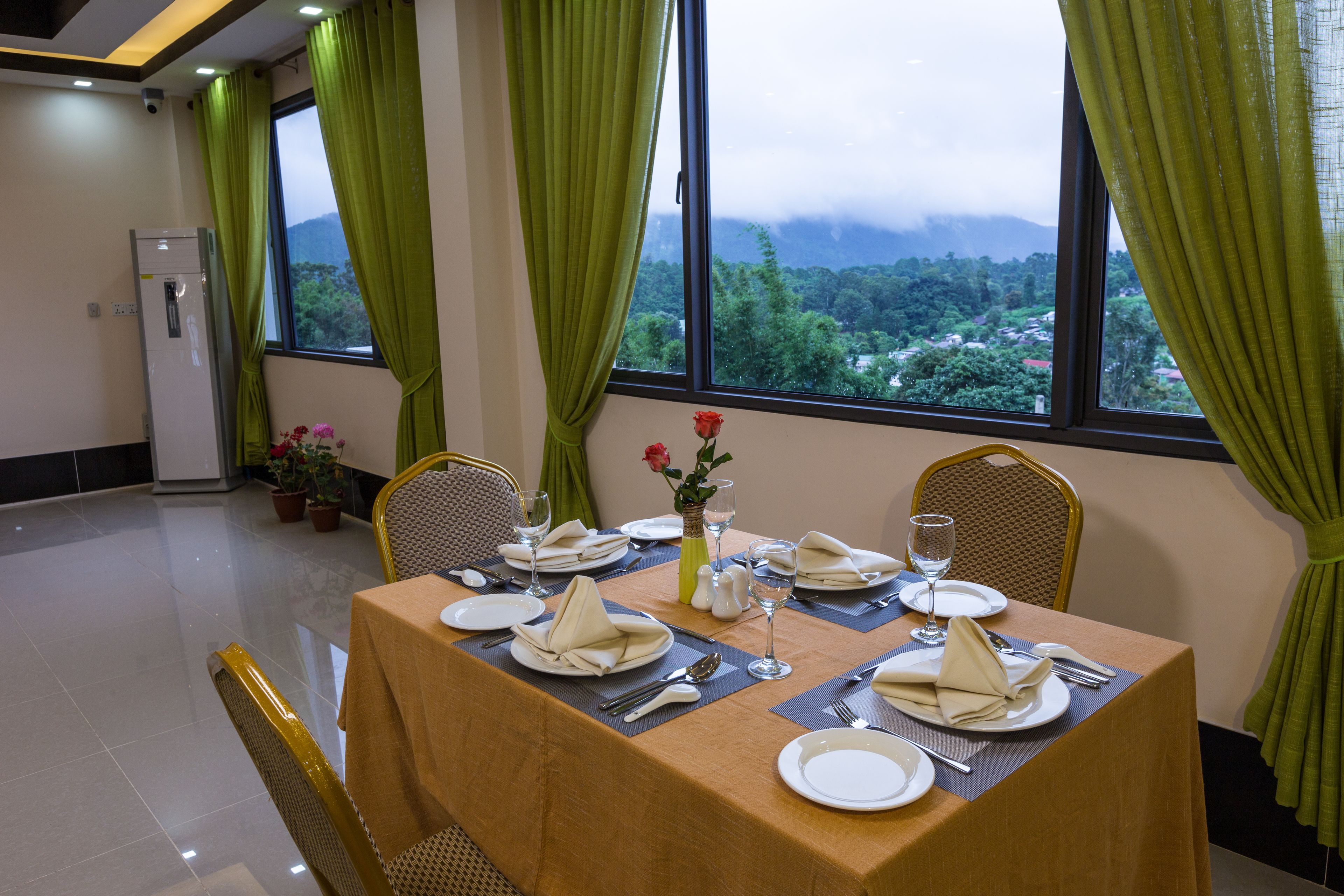 Une table à manger dressée pour quatre personnes, avec vue sur un paysage montagneux grâce à de grandes fenêtres.