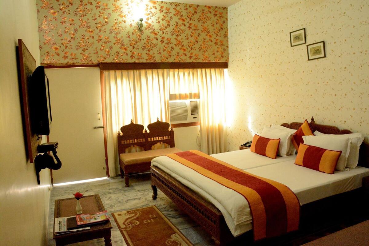 Une chambre d’hôtel avec un lit, une chaise, une petite table, un téléviseur et une fenêtre avec des rideaux.