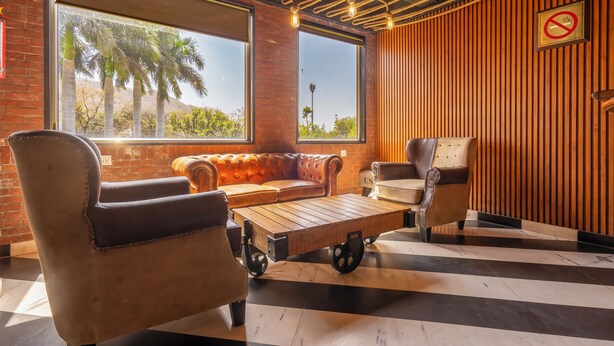 Un salón moderno con sofás de cuero, una mesa de centro de madera y vistas a palmeras a través de amplias ventanas.