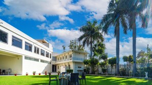 Un edificio moderno con un área de estar al aire libre techada, palmeras y cielo despejado.
