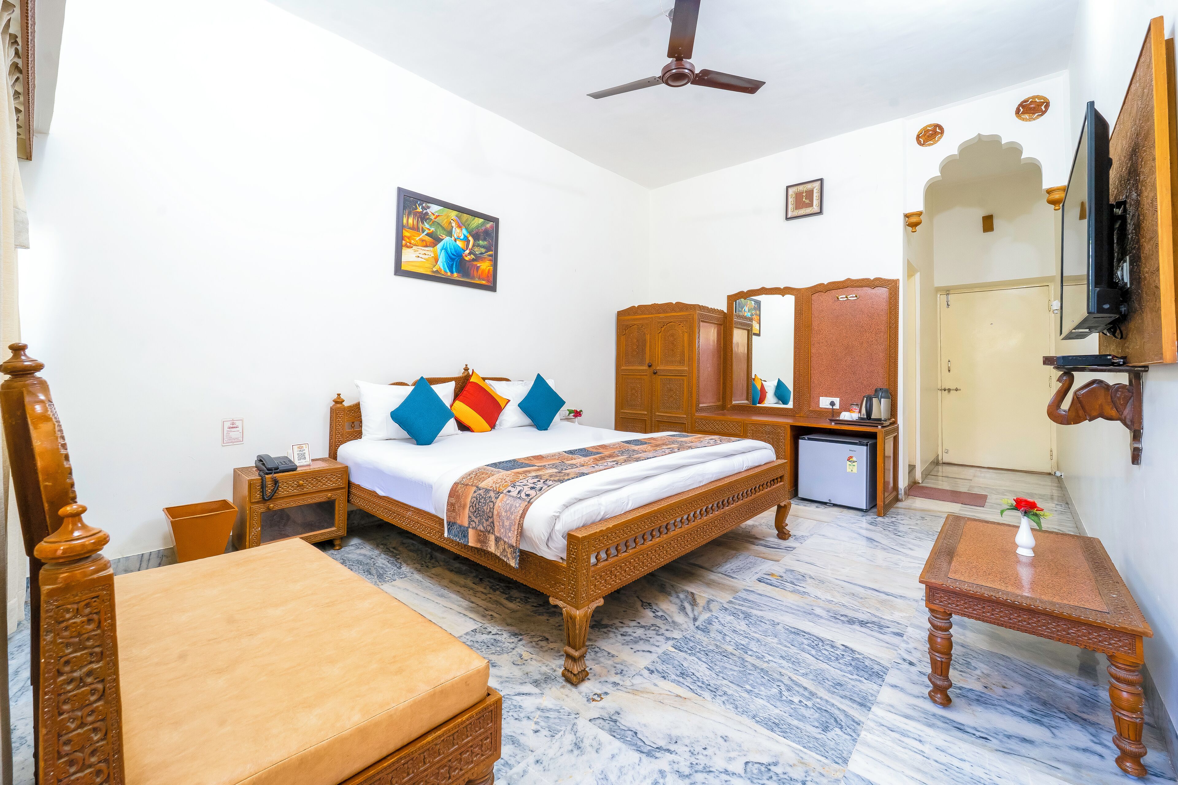 A hotel room with a wooden bed, a small desk, a television, and a ceiling fan.