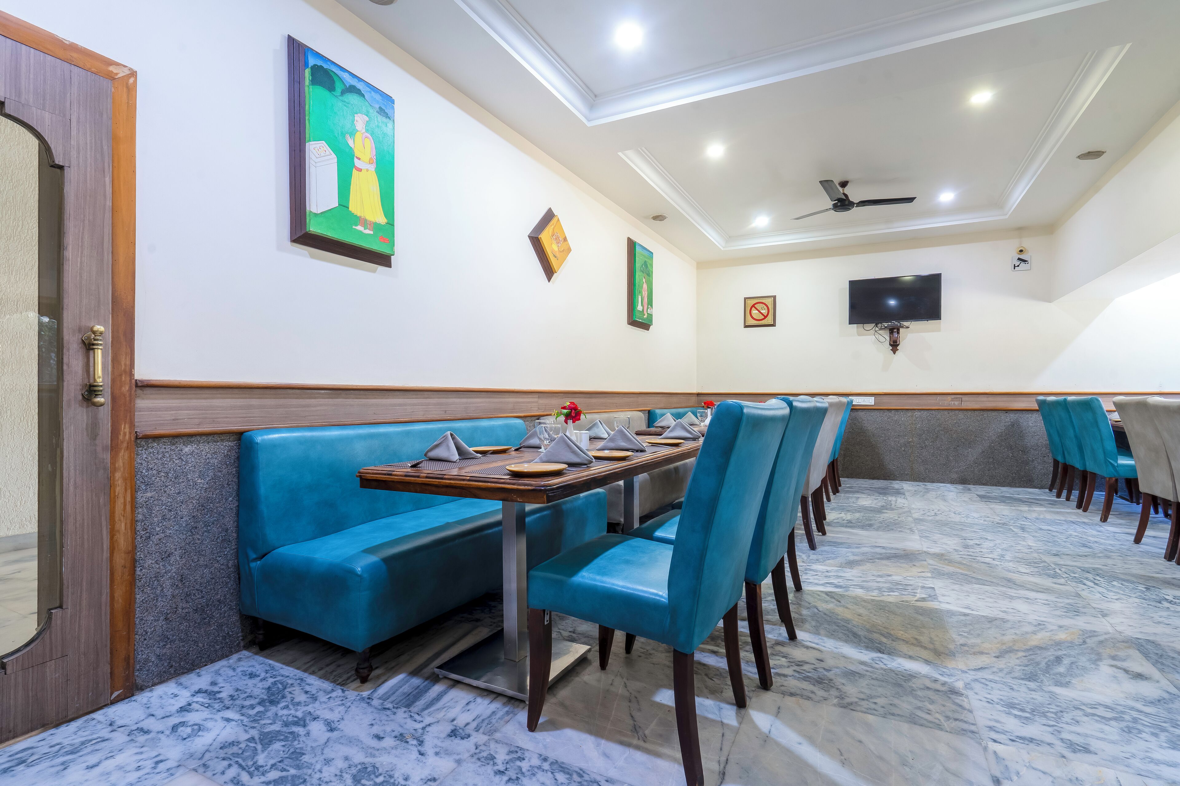 Restaurante com assentos em azul, piso de mármore e ventoinha no teto.