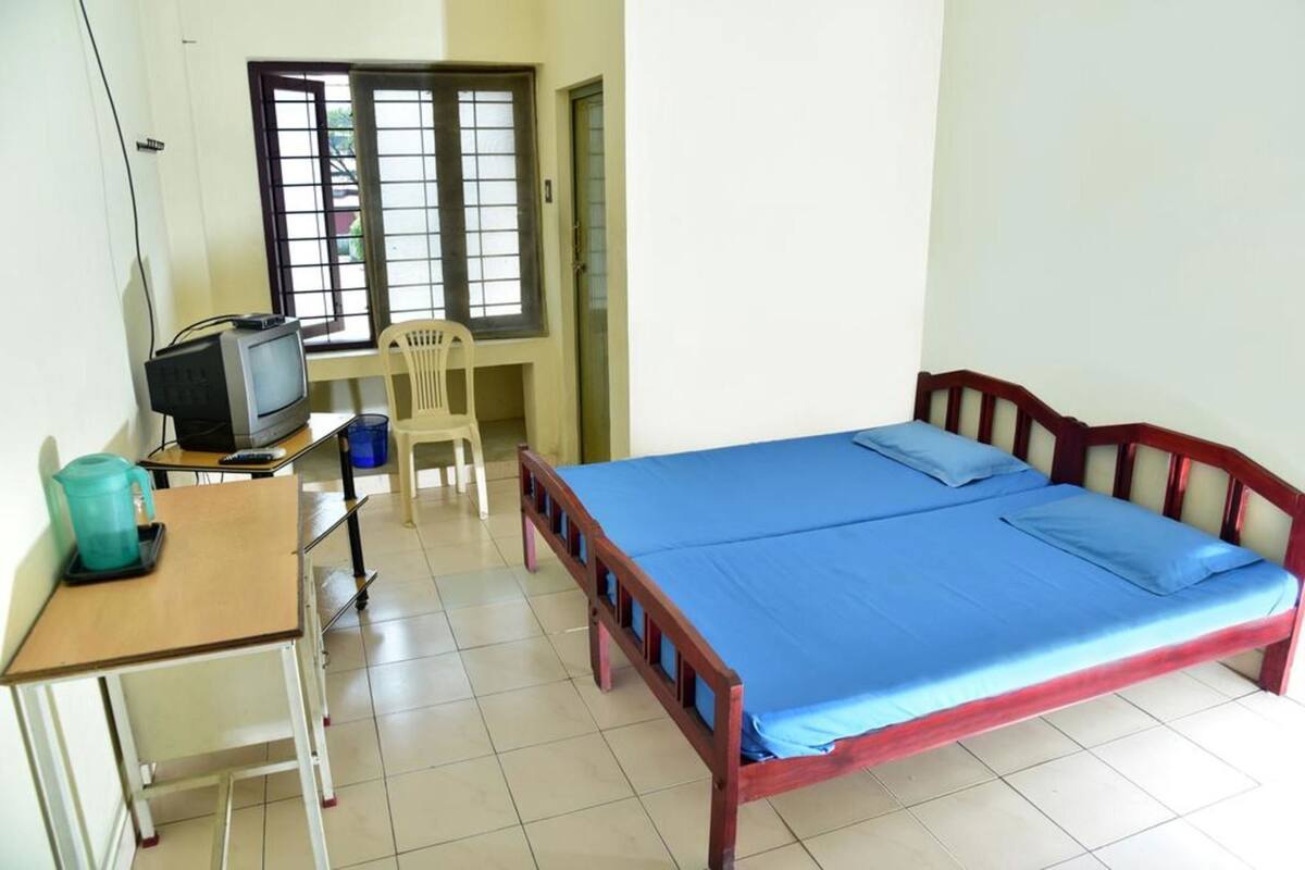 A room with a bed, a desk with a television, a chair, and a window with bars.