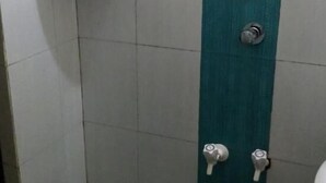 A small bathroom with a green and white tiled wall, a white sink, and a red fire extinguisher. - Sithara Guest House (Palakkad)