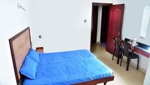 A single bed with a blue mattress and wooden headboard in a room with white walls and a tiled floor. - Sithara Guest House (Palakkad)