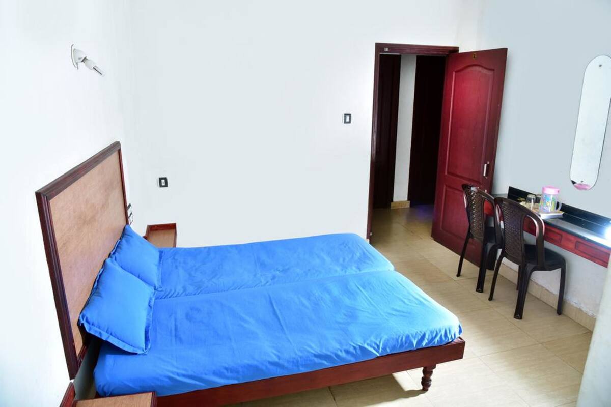 A single bed with a blue mattress and wooden headboard in a room with white walls and a tiled floor.