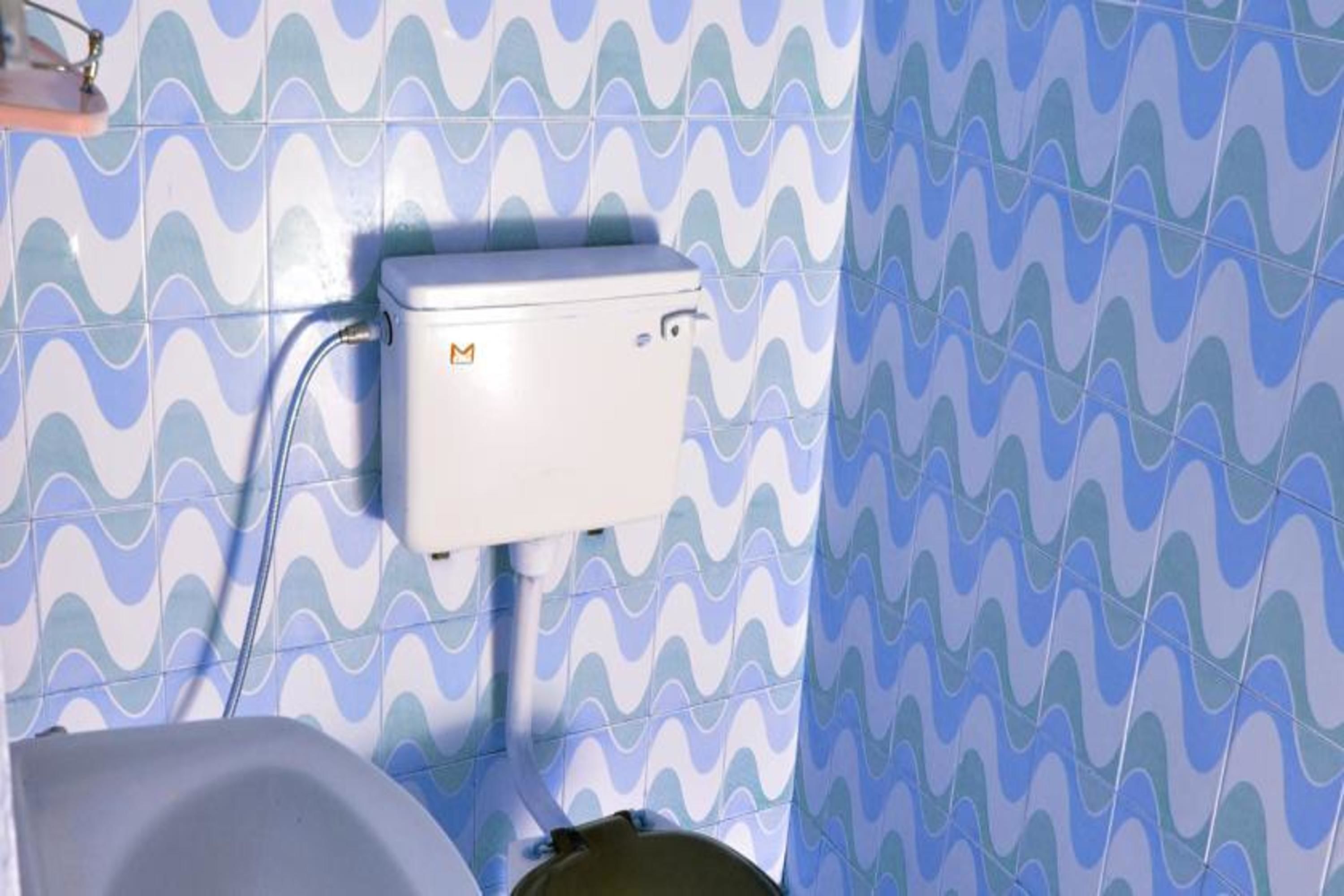 A bathroom with a toilet, a sink, and a shower. The walls have a wavy blue and white tile pattern.
