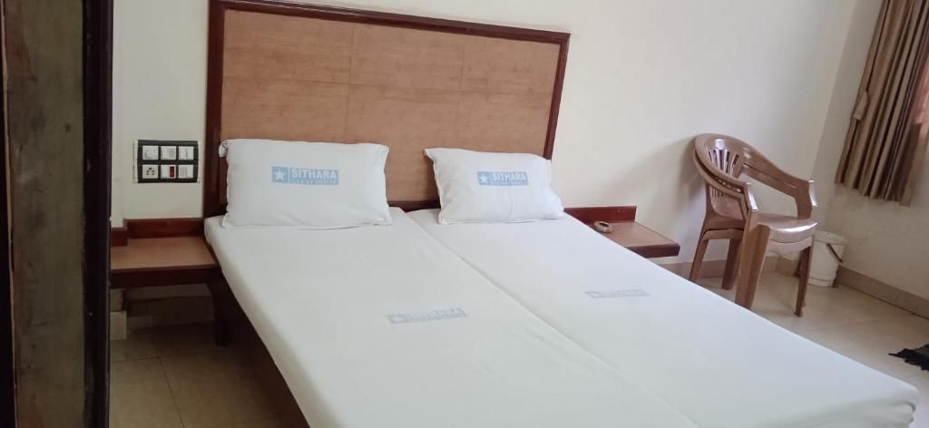 A double bed with a wooden headboard, two pillows, a wooden nightstand, and a wooden chair.