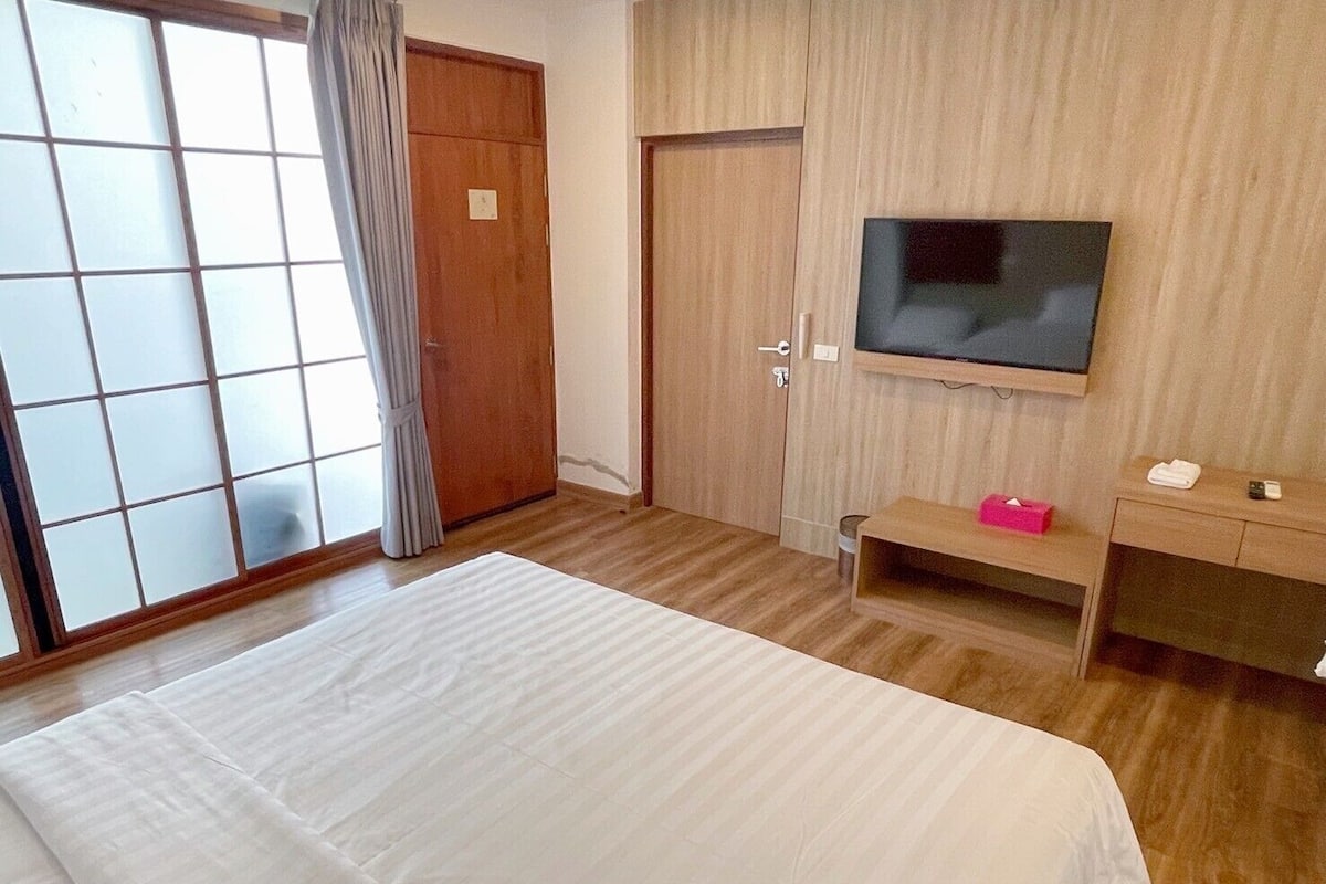 A hotel room with a large bed, a TV mounted on the wall, a wooden wardrobe, and a sliding glass door.