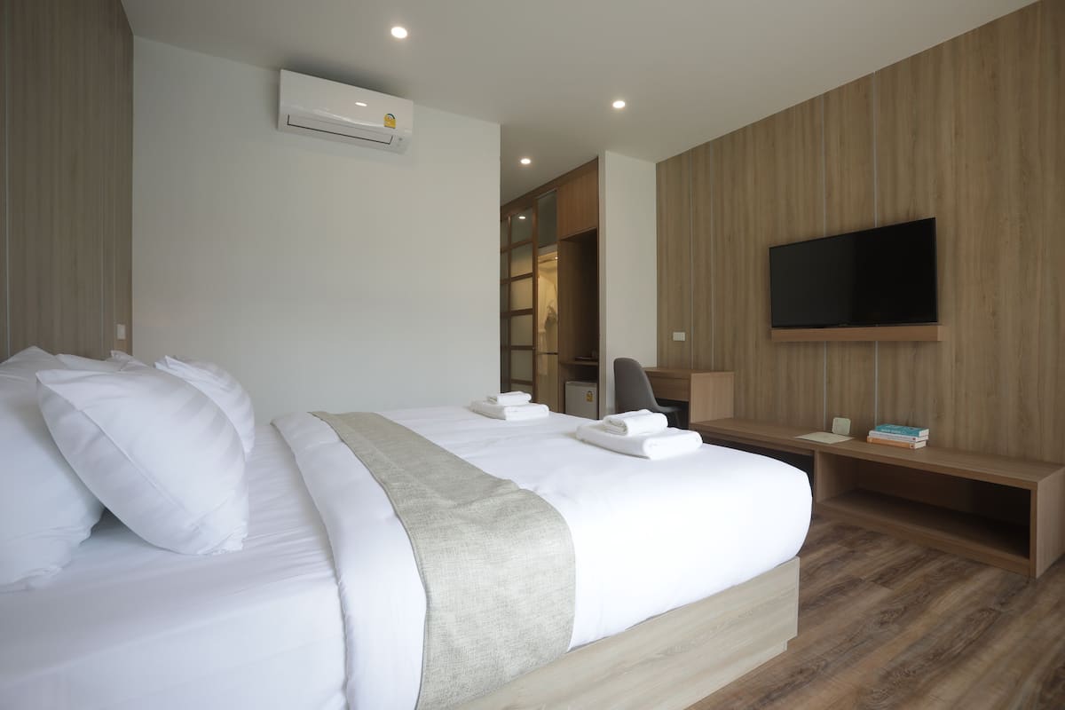 A modern hotel room with a large bed, a flat-screen TV mounted on the wall, a desk, and a built-in wardrobe.