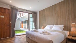 A modern hotel room with a large bed, wooden flooring, and a view of a building through a glass door. - Kyoto Great Hotel (Chiang Mai)