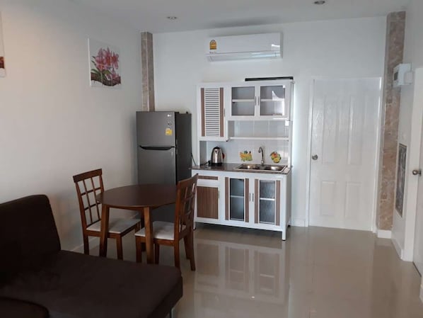 A compact kitchen with a refrigerator, a sink, and a cabinet. There is a dining table with chairs.
