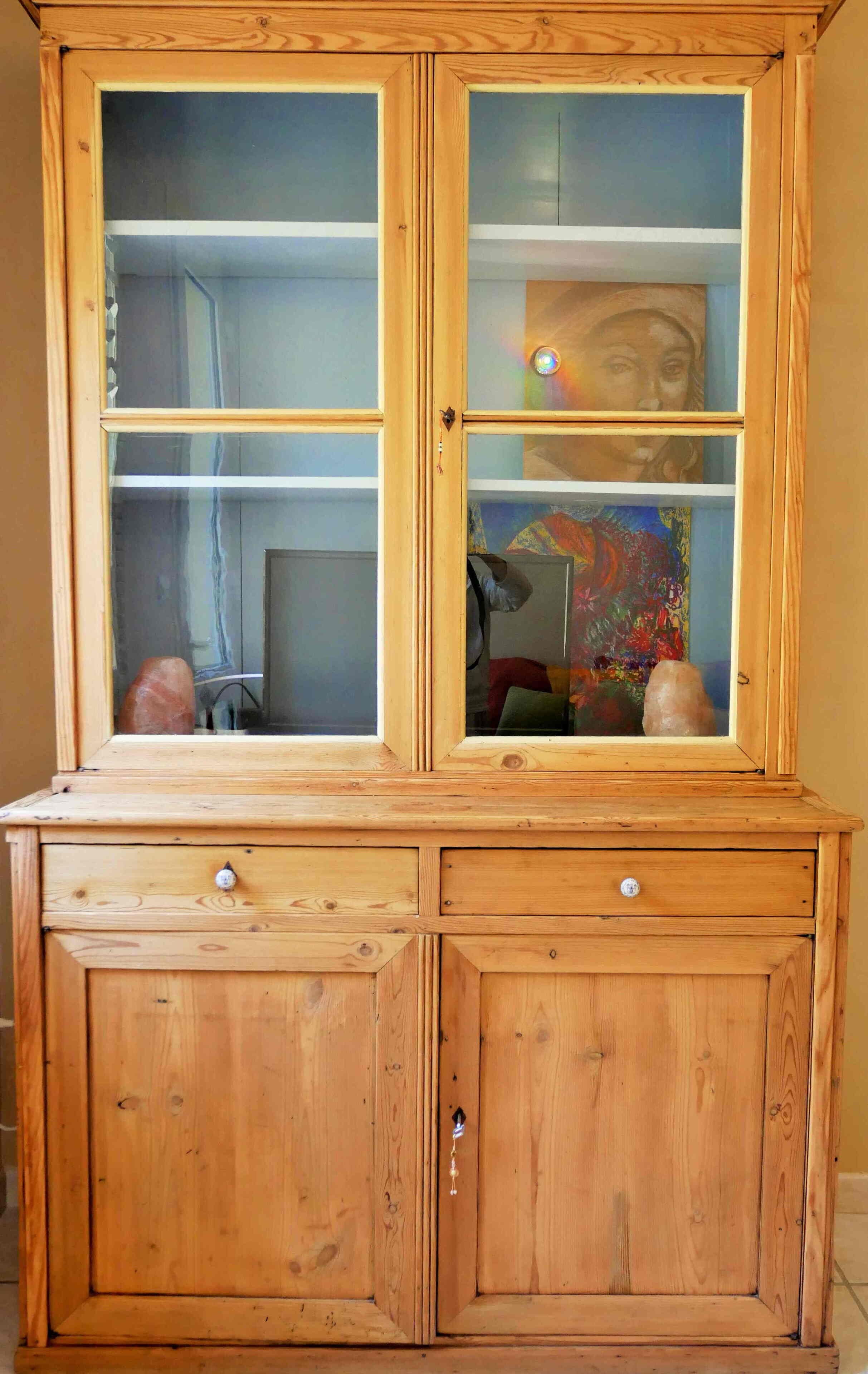 Un armari de fusta amb portes de vidre, amb dos calaixos i una prestatgeria.