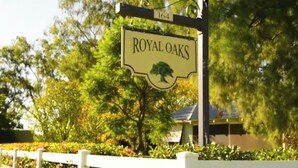 A sign for 'ROYAL OAKS' with a tree symbol, a number '164' above it, and a white fence in the foreground.