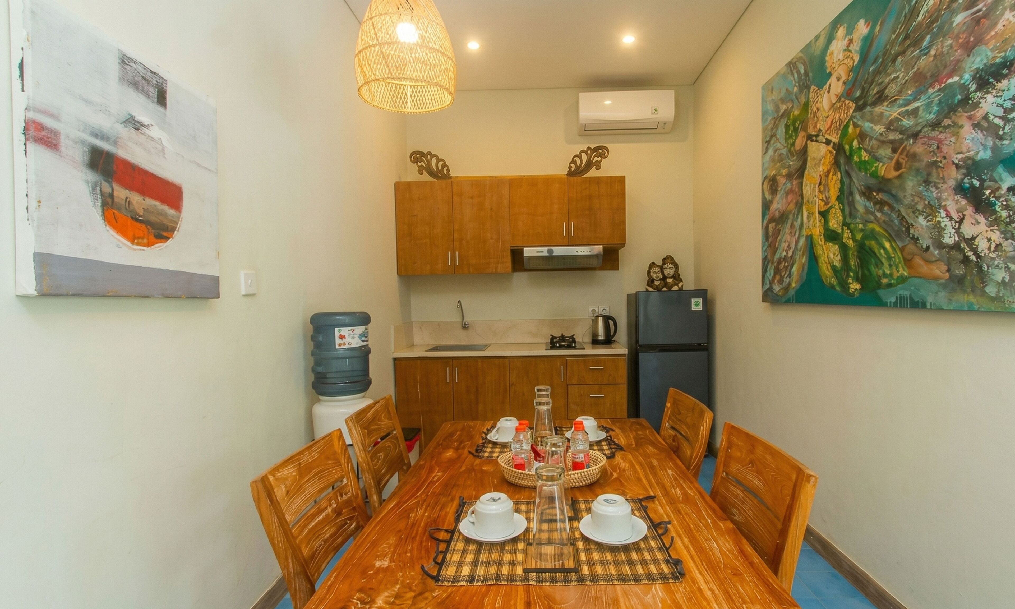 Un coin repas avec une table en bois, des chaises, un distributeur d’eau, un réfrigérateur et un tableau accroché au mur.