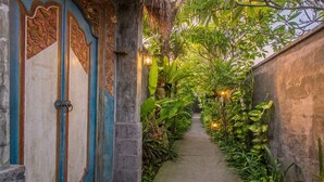 Un sendero estrecho bordeado por puertas decorativas y abundante vegetación, que conduce a un edificio de fachada de piedra.