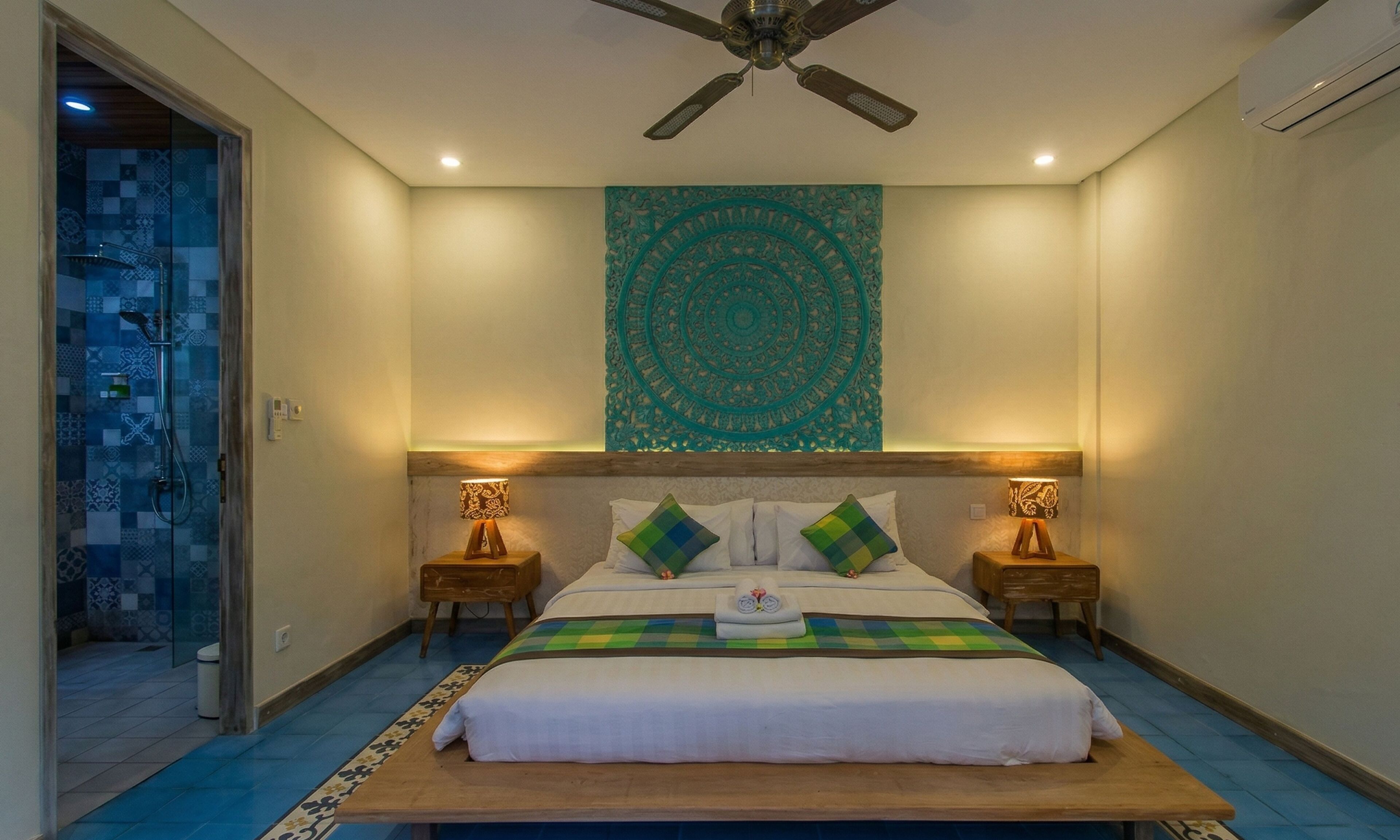A hotel room with a bed, two bedside lamps, a ceiling fan, and a decorative tapestry.