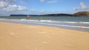 A beach with a boat in the water, a sandy shore, and a distant hill. - Eden Rock is an immaculately presented bungalow situated in the heart of Rock. (Rock, Wadebridge)