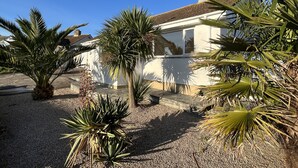 A house with a white exterior, surrounded by palm trees and a gravel driveway. - Eden Rock is an immaculately presented bungalow situated in the heart of Rock. (Rock, Wadebridge)