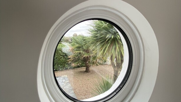 A window with a view of a garden and a sign that reads "BEACH". - Eden Rock is an immaculately presented bungalow situated in the heart of Rock. (Rock, Wadebridge)
