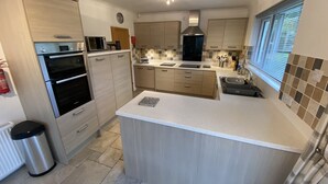 A modern kitchen with a central island, built-in oven, microwave, and a large window providing natural light. - Eden Rock is an immaculately presented bungalow situated in the heart of Rock. (Rock, Wadebridge)